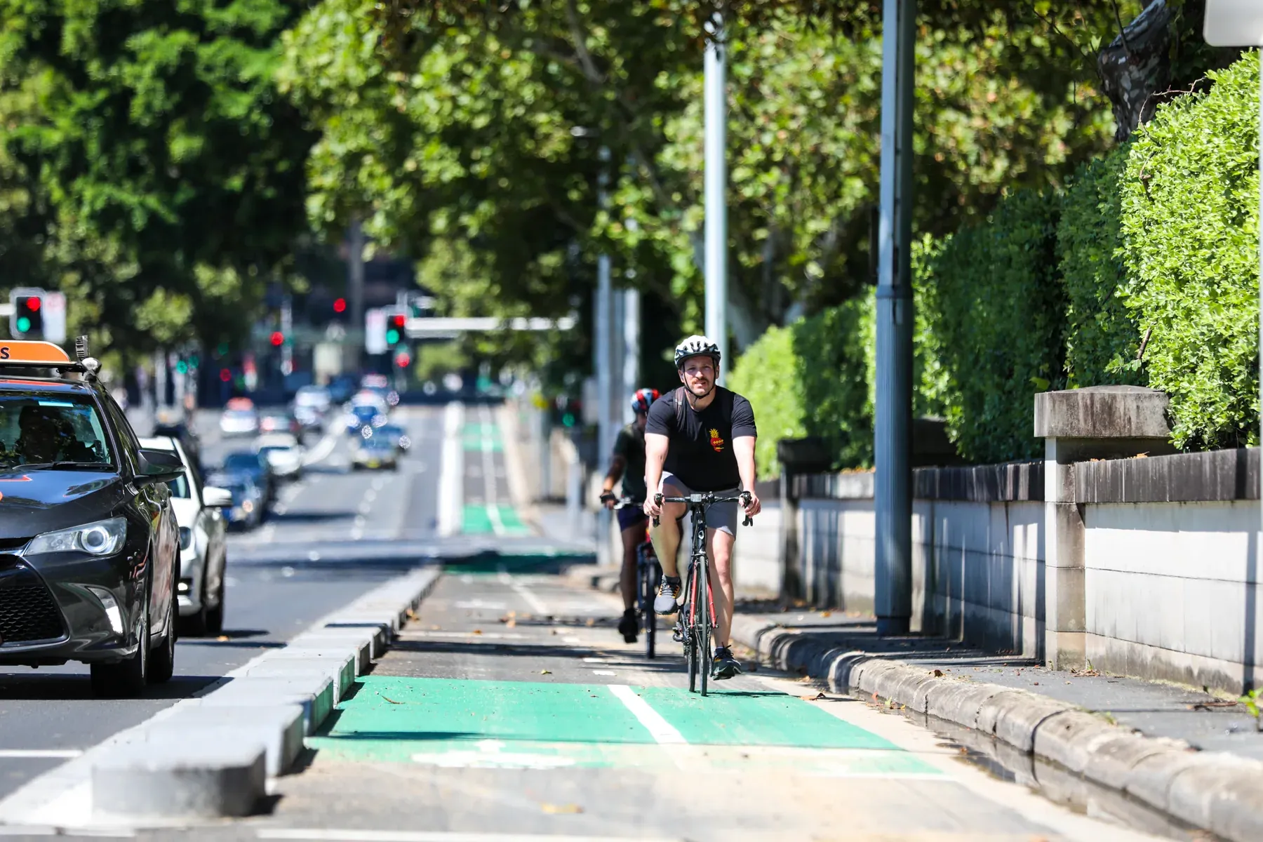A cyclist riding within a protected green cycle lane on a Sydney street.